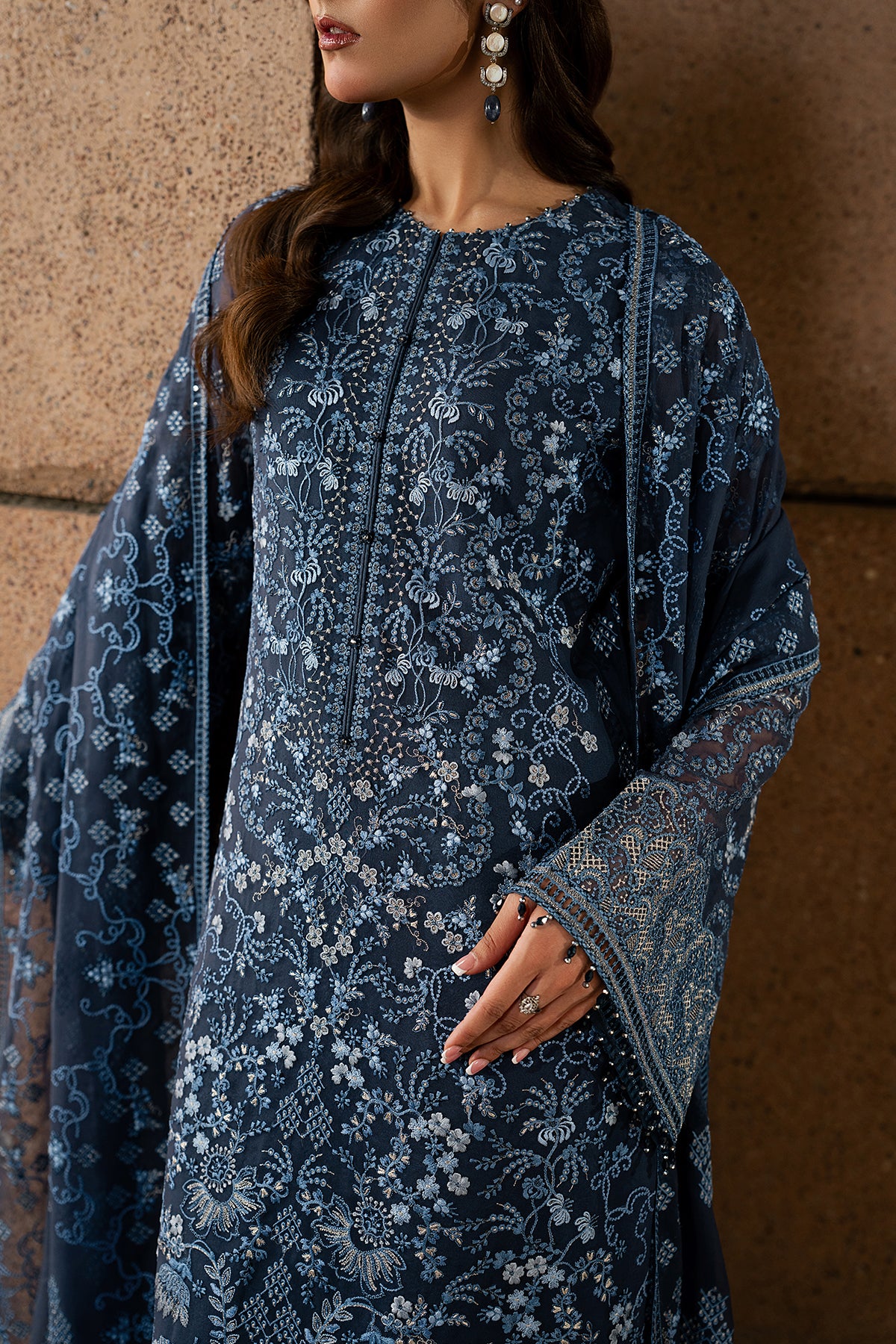 Woman wearing a blue embroidered traditional outfit against a brown background