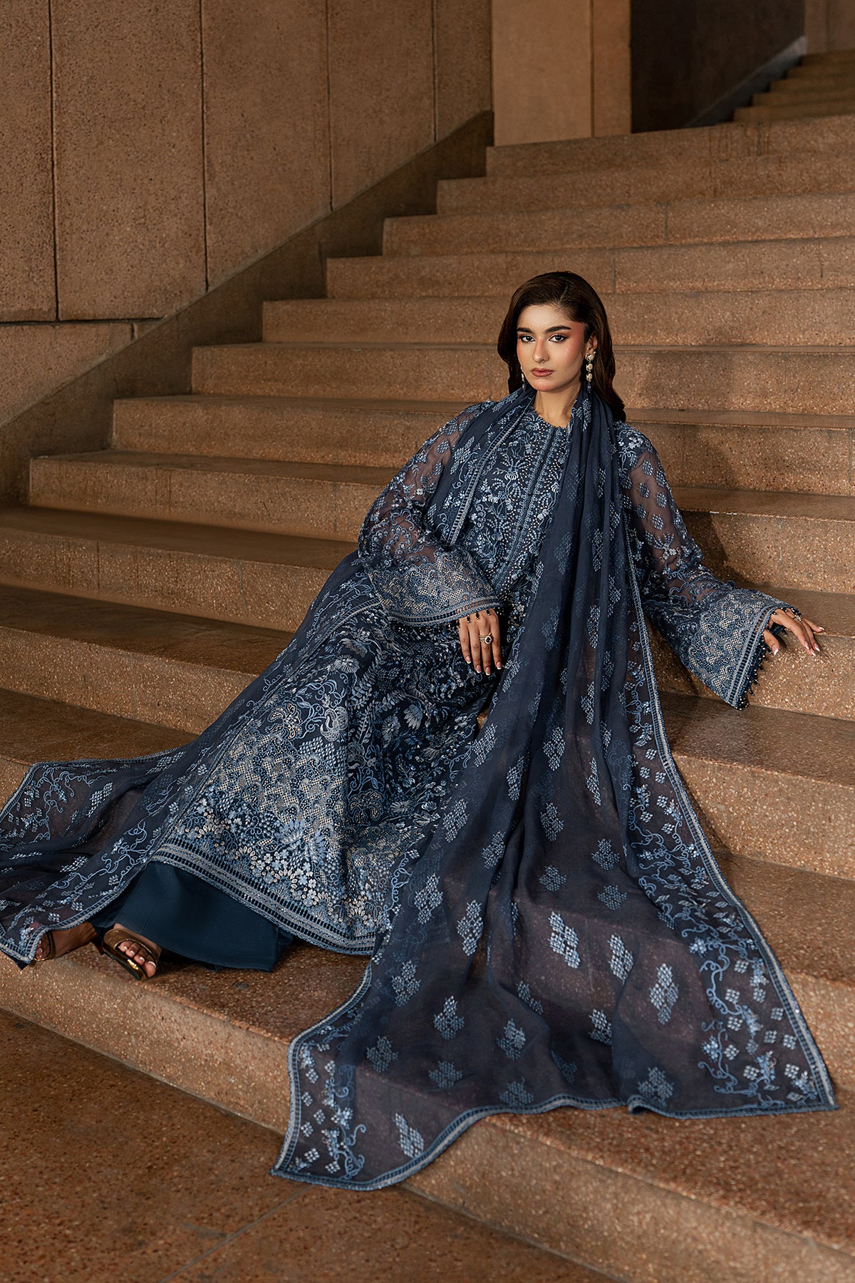 Woman in a blue embroidered dress sitting on a staircase.