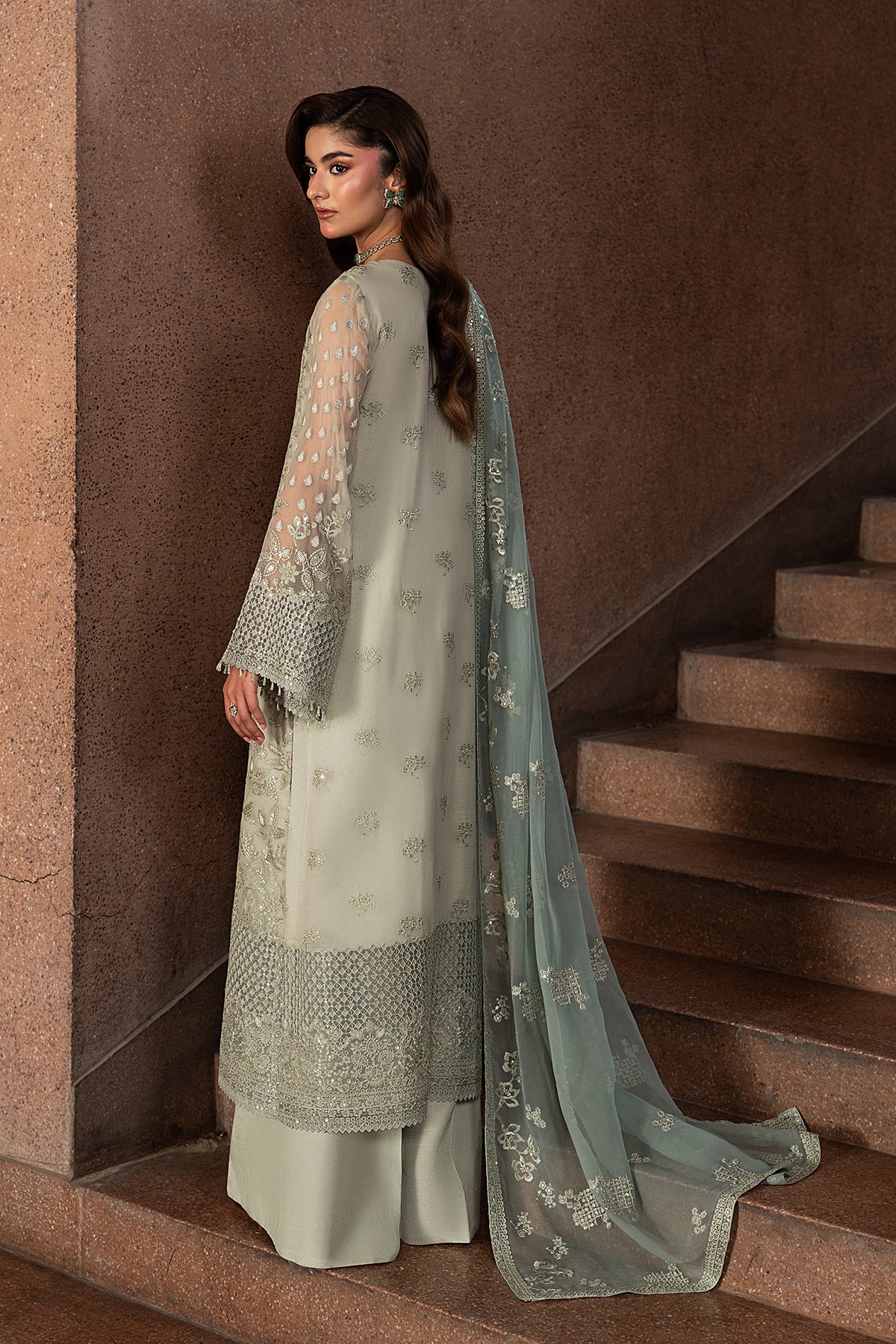 Woman in traditional outfit standing on a staircase with a brown wall background