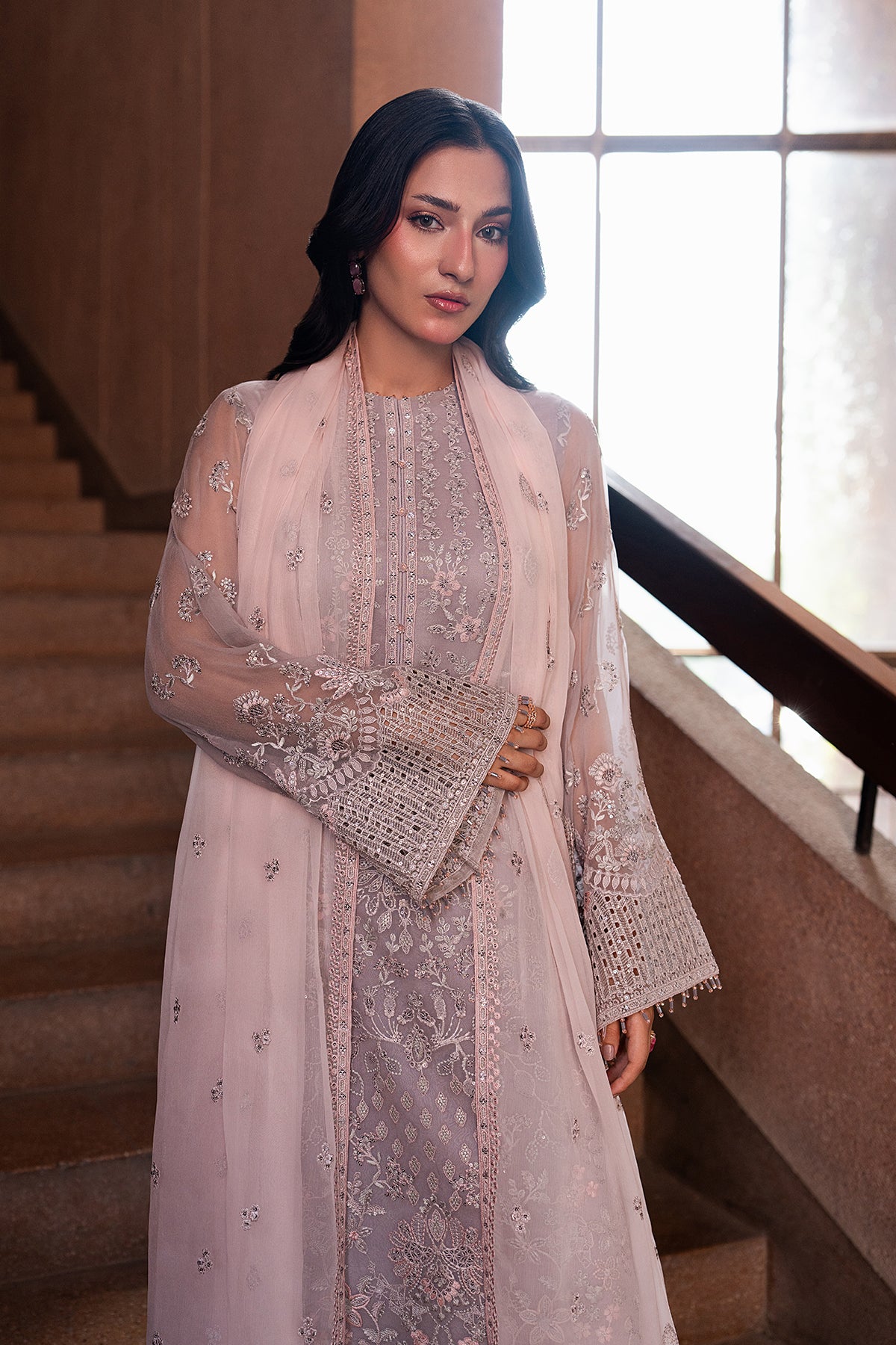 Woman in an elegant outfit standing in a well-lit room with a staircase.