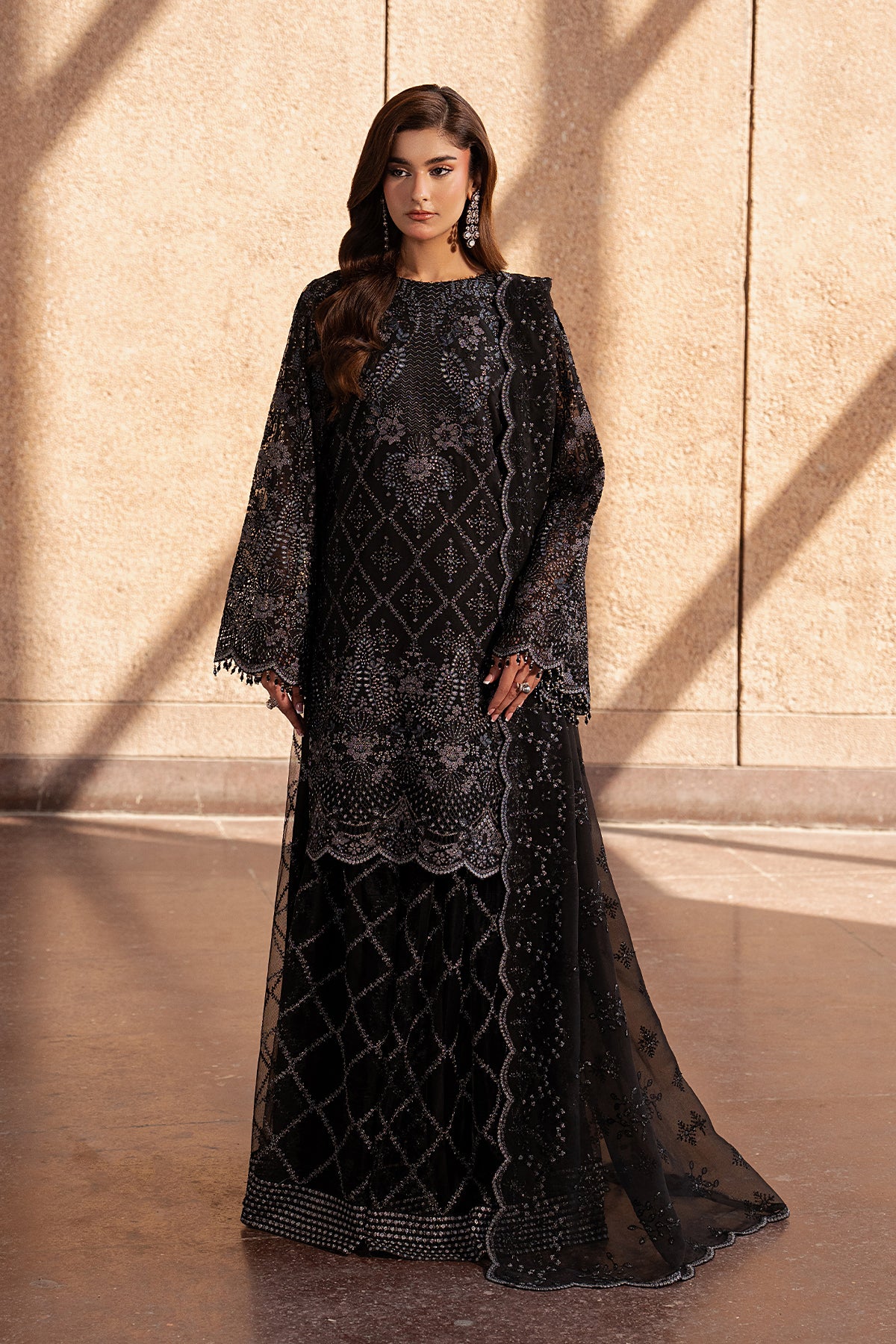 Woman wearing a black embroidered dress against a beige wall.