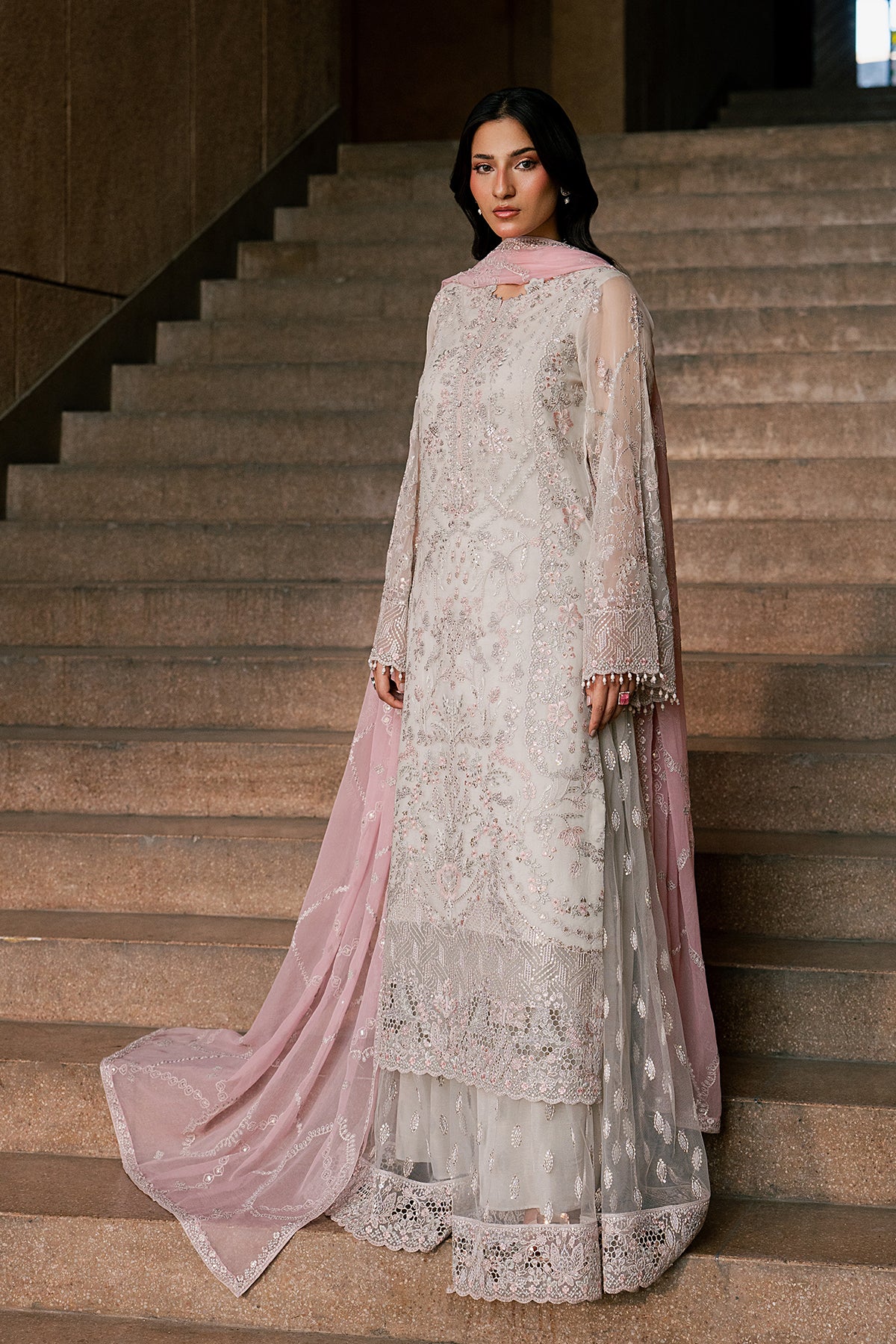 Woman in a light-colored embroidered outfit standing on a staircase