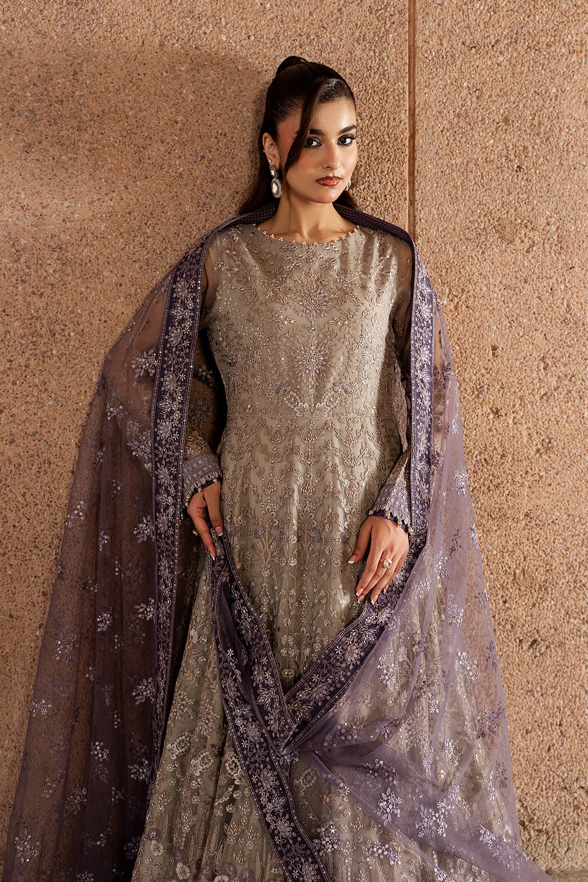 Woman wearing a silver traditional outfit with a dark dupatta against a beige wall.