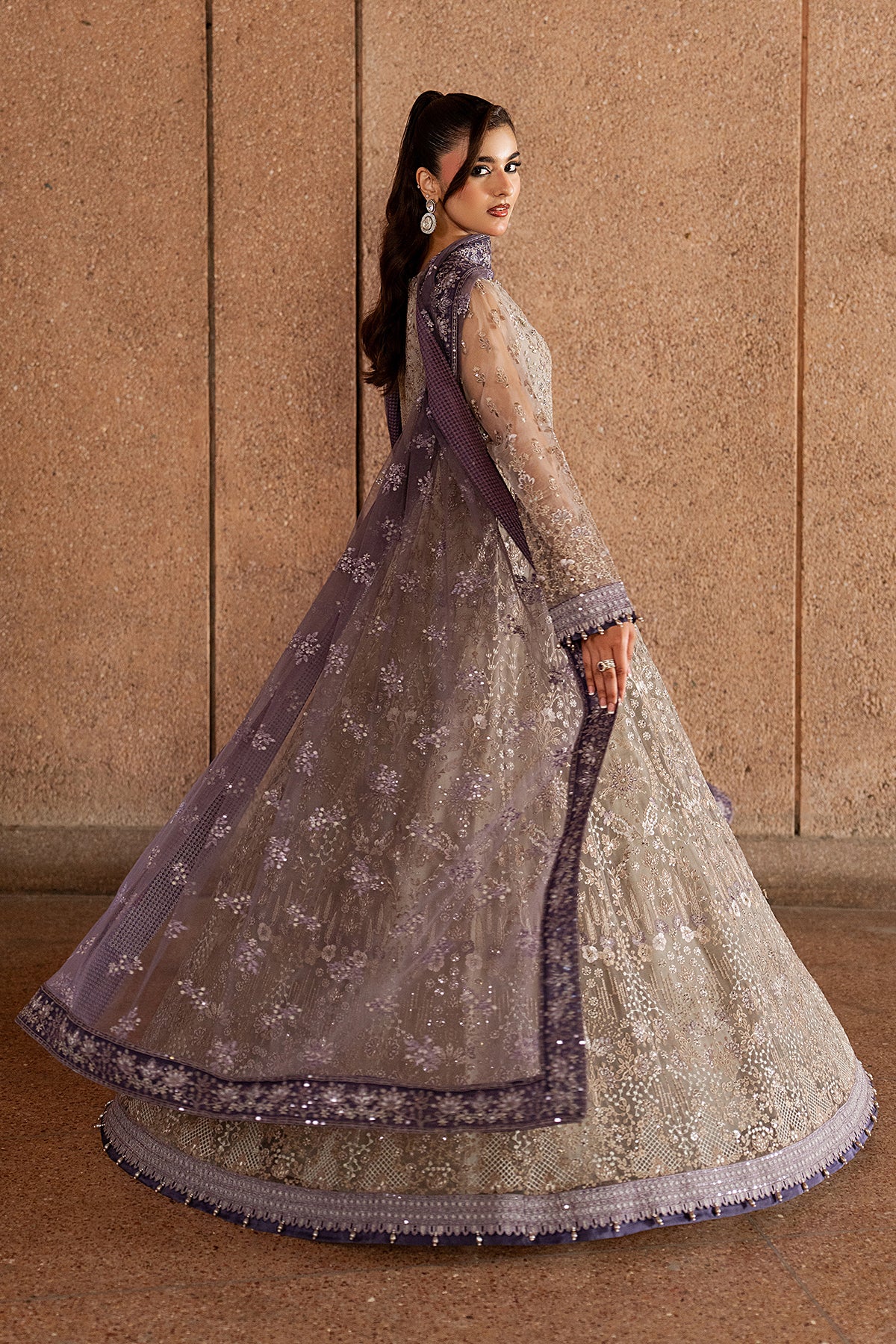 Woman in a traditional embroidered outfit against a beige wall.