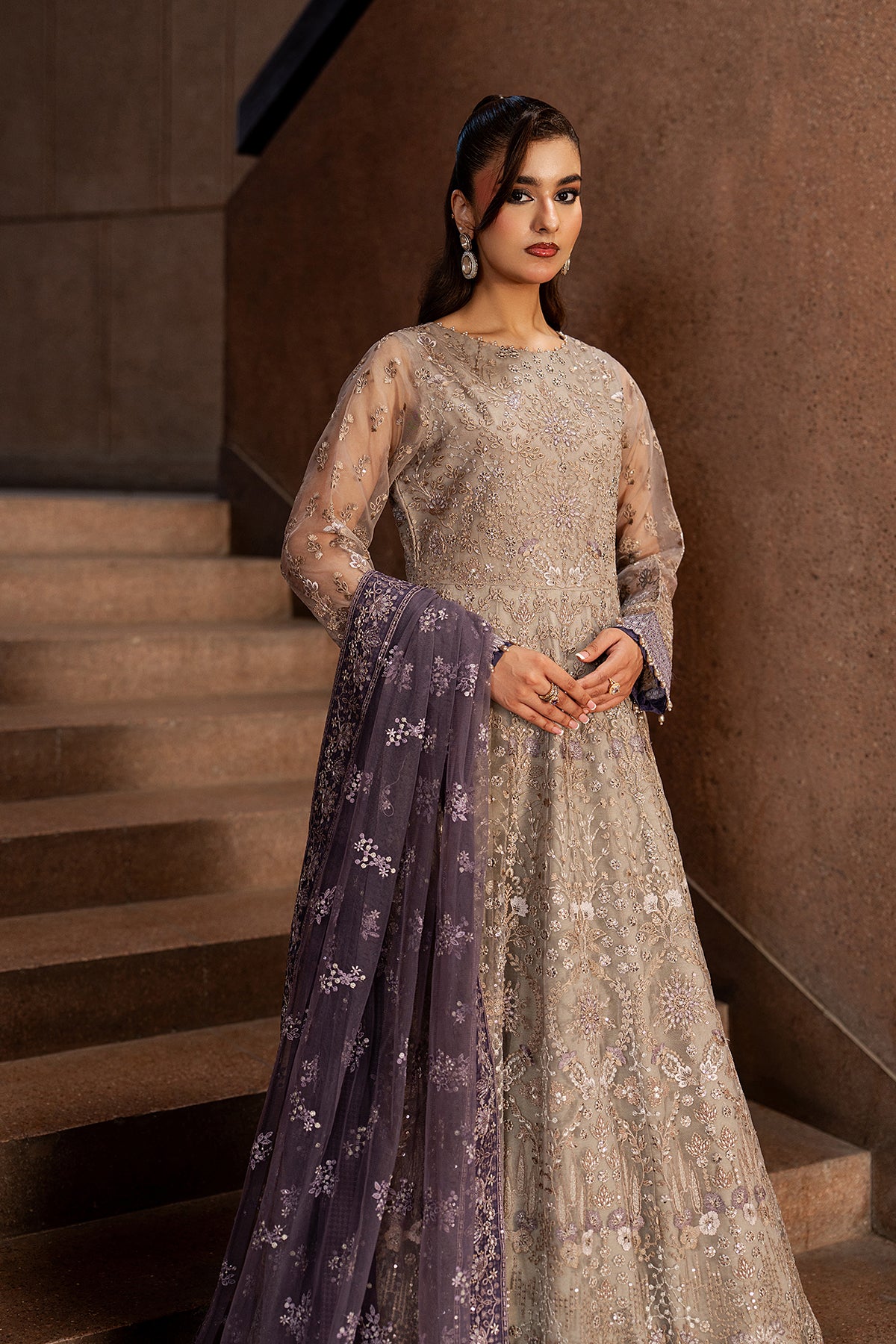 Woman in a silver embroidered outfit with a purple dupatta standing on a staircase.