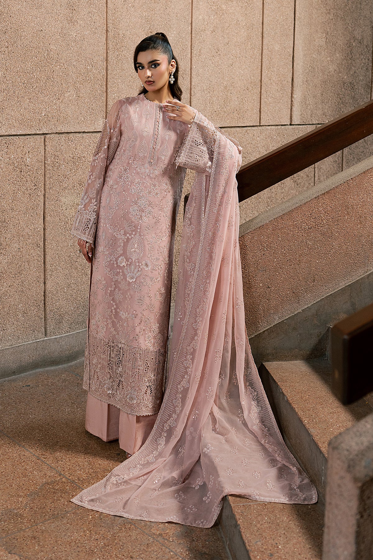 Woman in a pink embroidered outfit standing on a staircase.