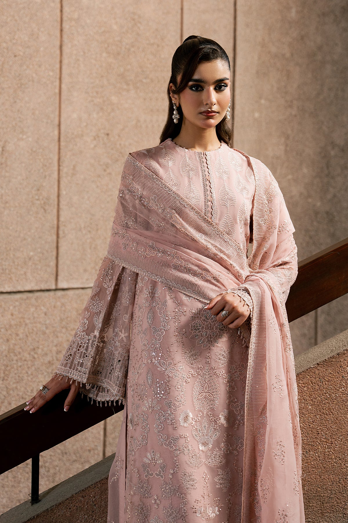 Woman wearing a pink embroidered traditional outfit against a beige wall.