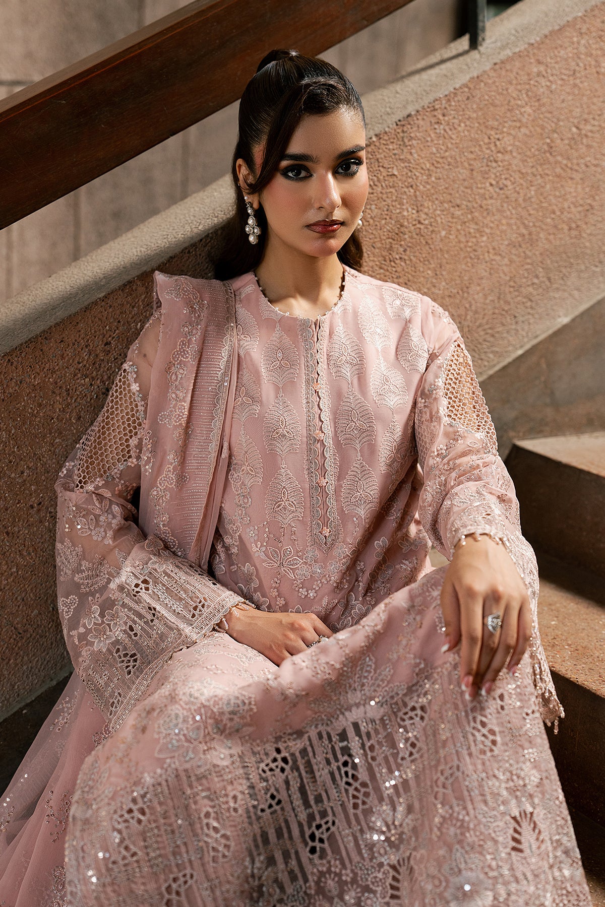 Woman in a pink embroidered outfit sitting on steps.