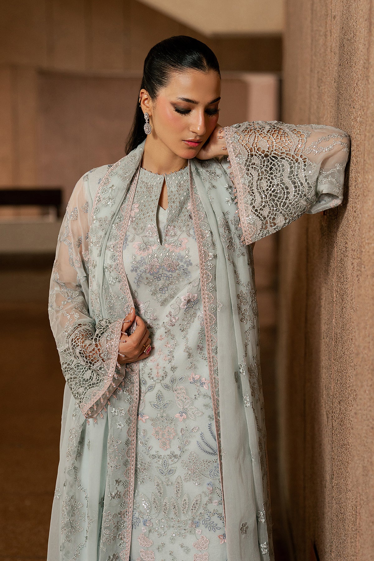 Woman in a light gray traditional outfit with intricate patterns, standing against a neutral background.