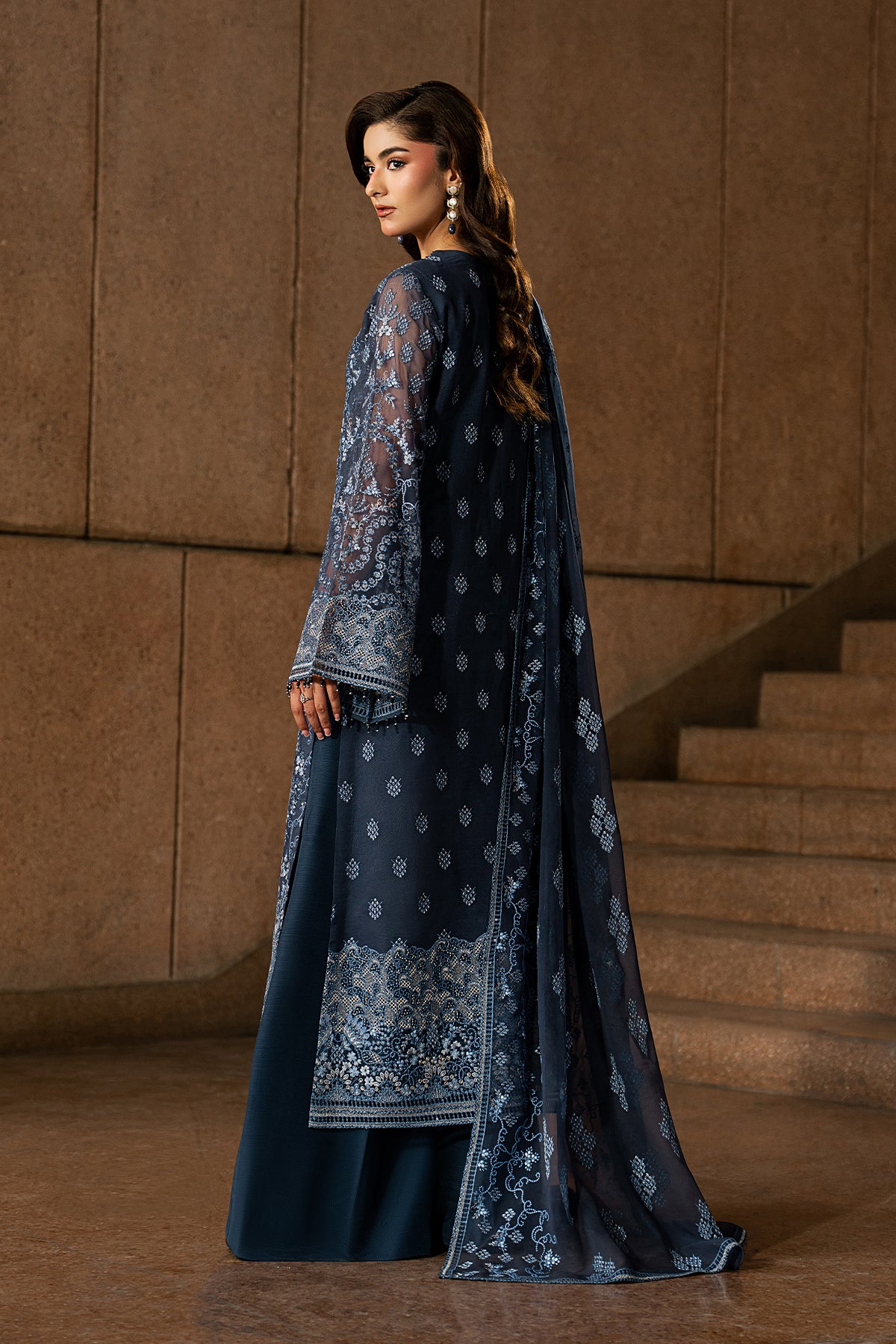 Woman in a dark blue embroidered traditional outfit standing in front of a textured wall.