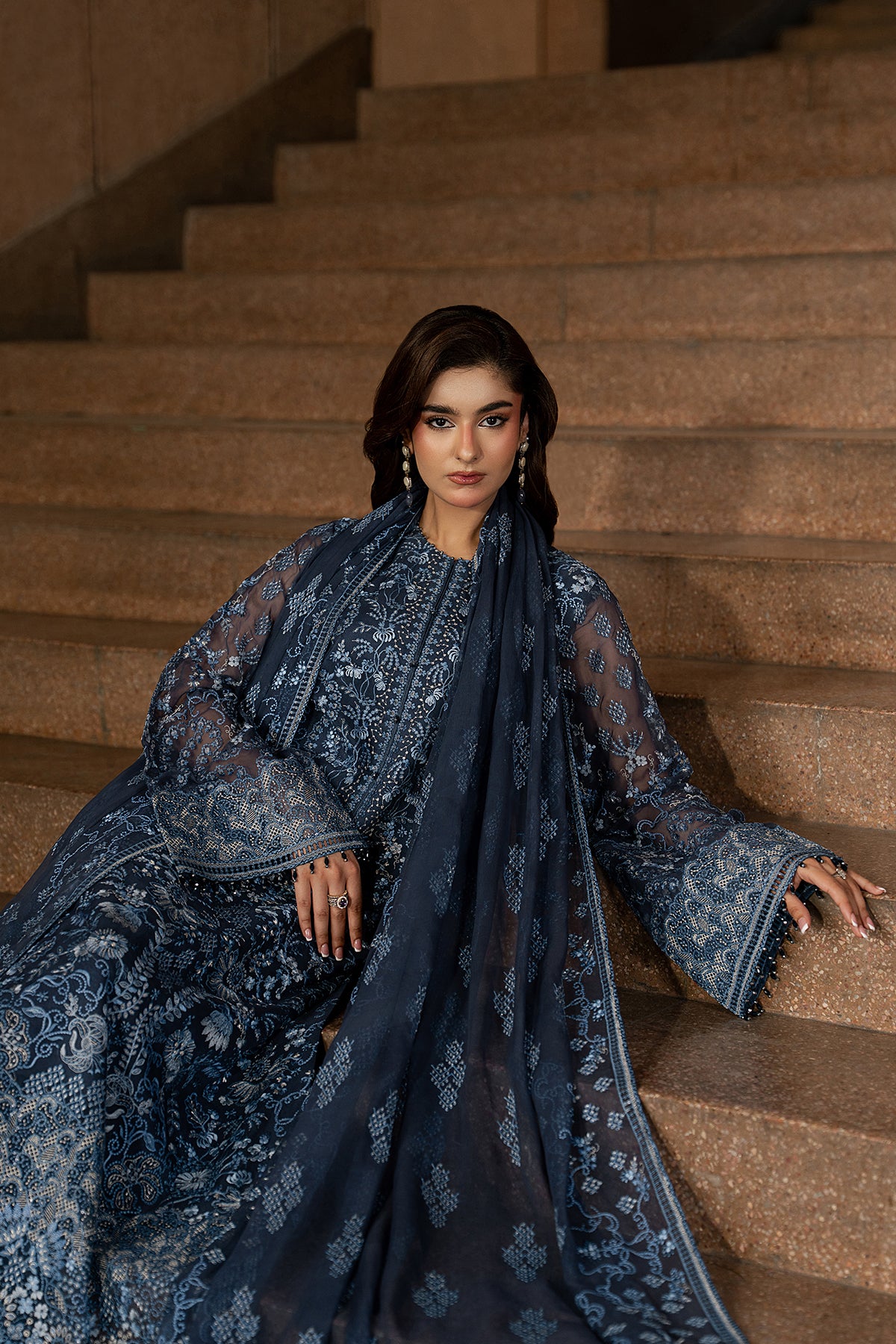 Woman in a blue embroidered traditional outfit standing on a staircase.