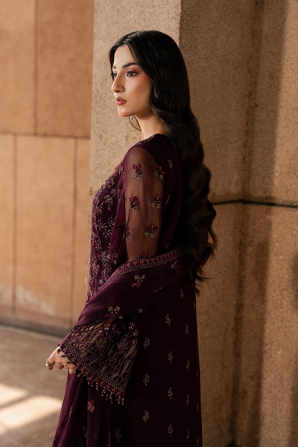 Woman in a dark purple dress with floral patterns standing against a textured wall.