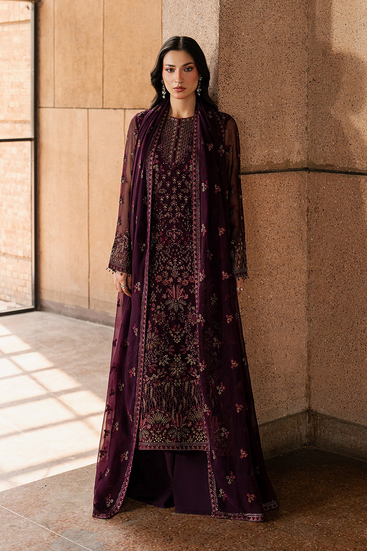Woman wearing a dark purple embroidered traditional outfit against a beige wall.