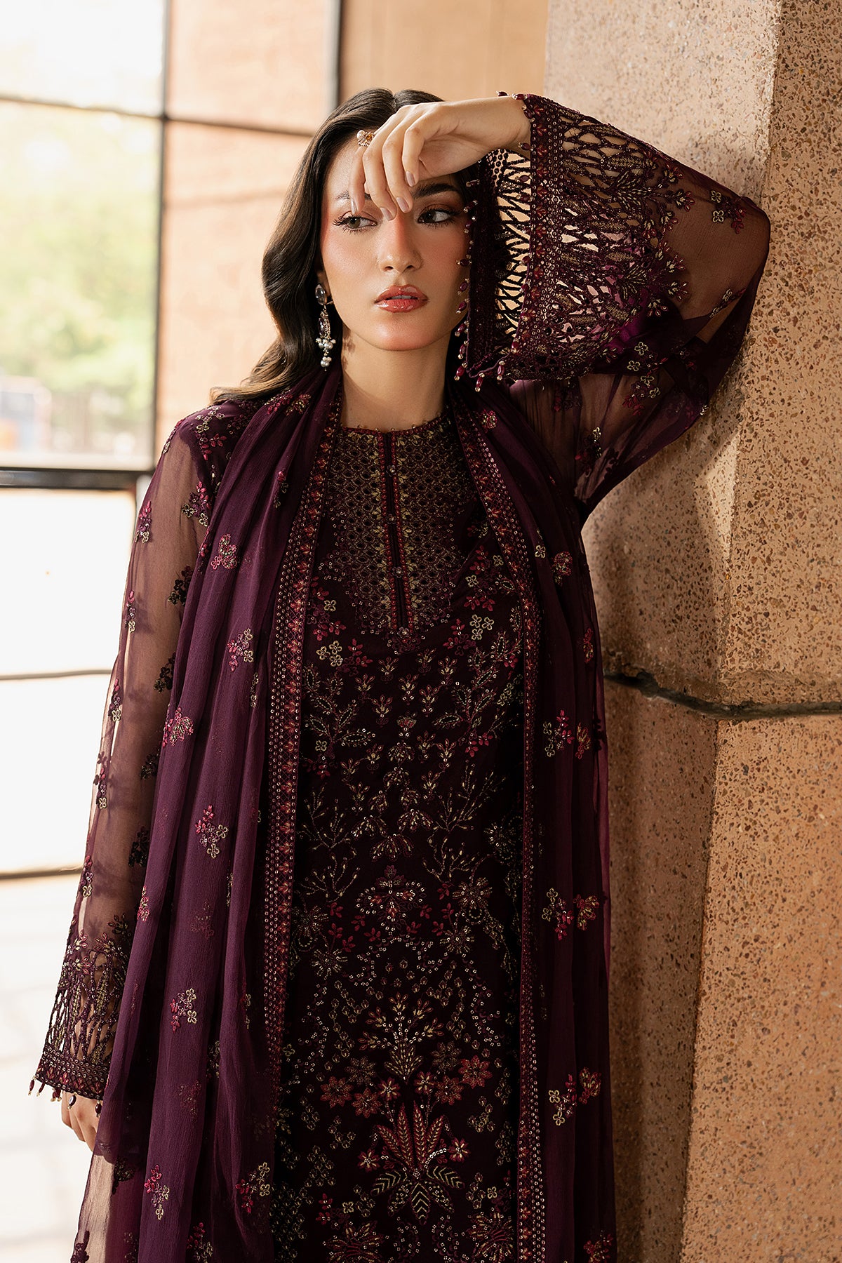 Woman in a dark purple floral outfit leaning against a stone wall.