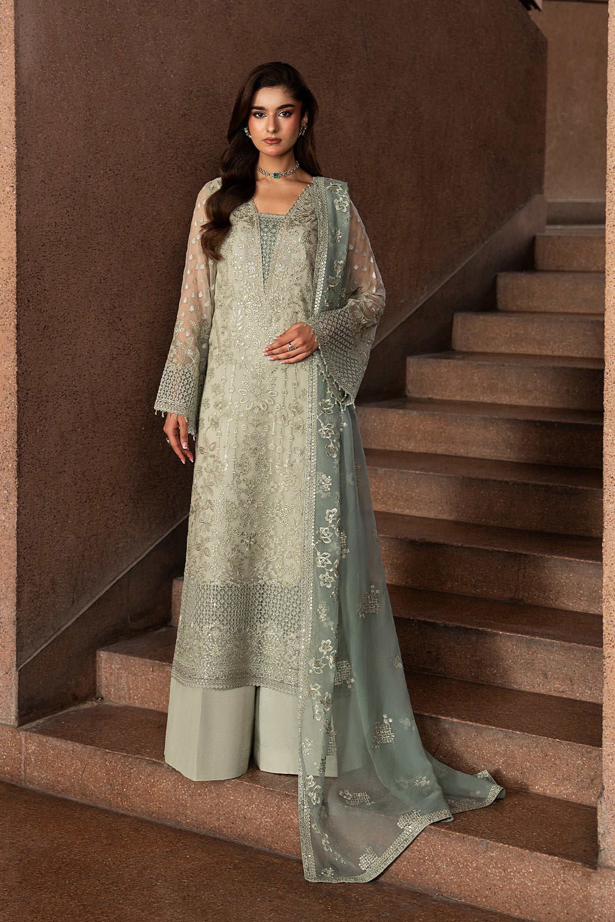 Woman in a light green embroidered outfit standing on a staircase.