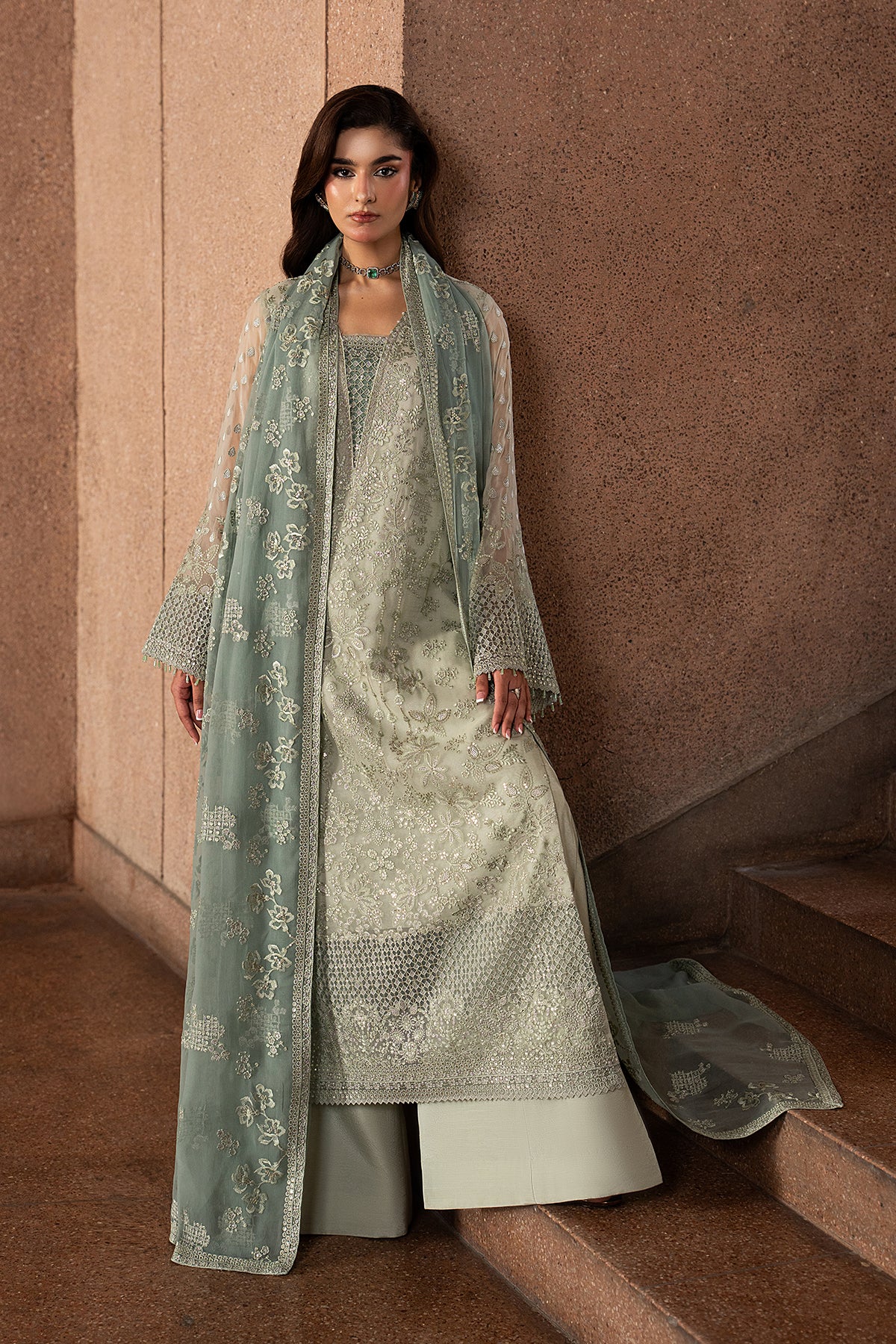 Woman in a traditional outfit with a light green dupatta standing on steps.