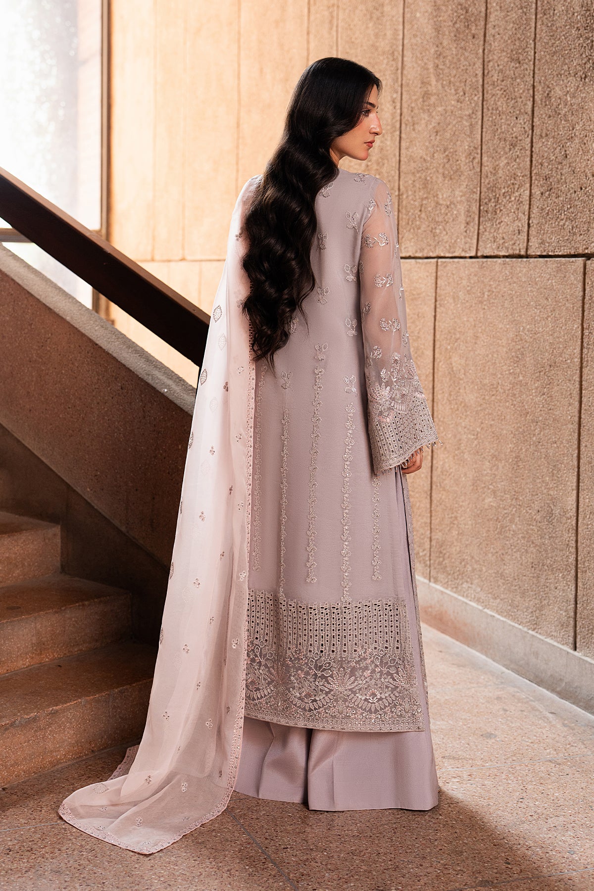Woman in a light purple traditional outfit standing in a modern indoor setting.