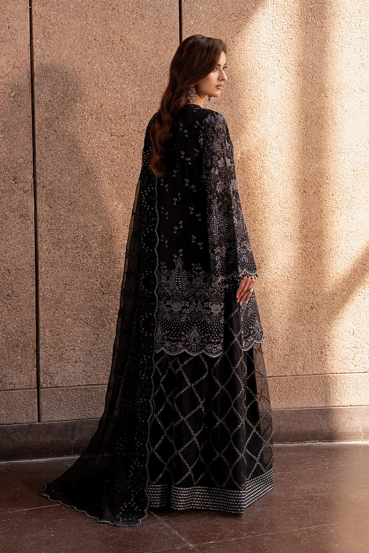 Woman wearing a black embroidered outfit standing against a textured wall.
