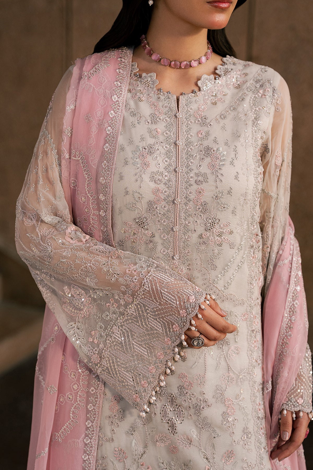 Woman wearing a light pink and white embroidered traditional outfit with a blurred background