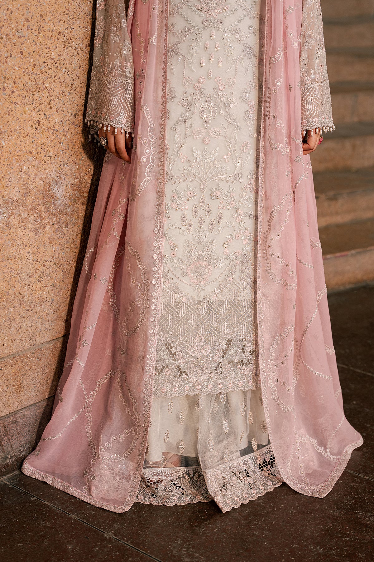 Delicate pink and white embroidered traditional outfit against a textured wall.