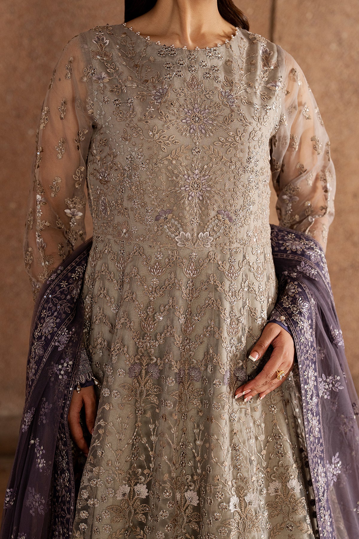 Woman wearing a detailed embroidered dress with a matching shawl against a neutral background