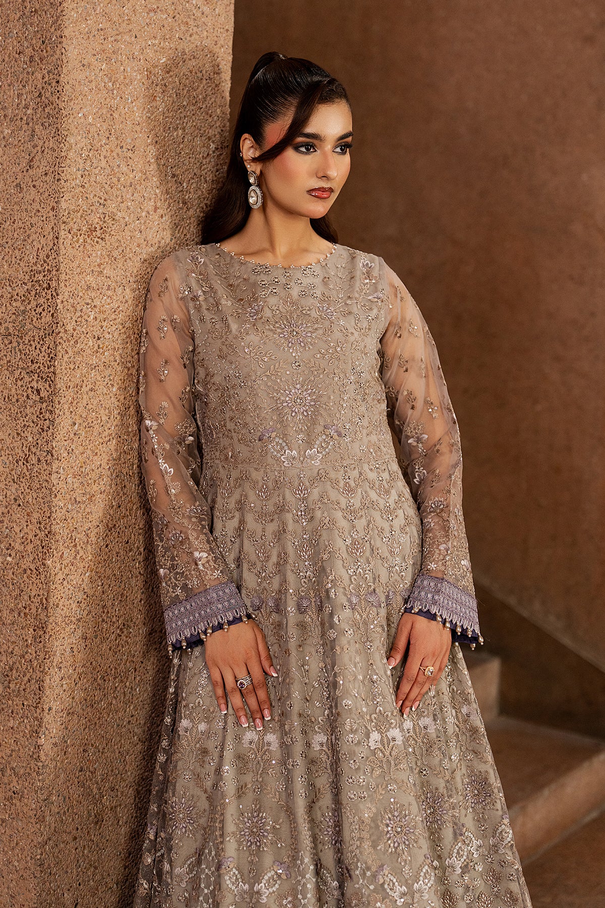 Woman wearing a detailed traditional outfit against a textured wall.