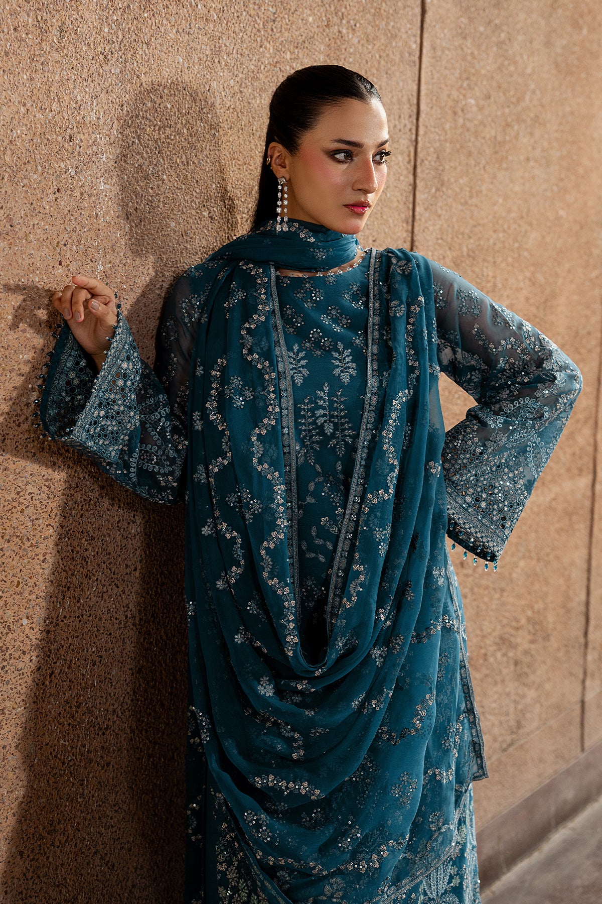 Woman wearing a blue embroidered outfit against a beige wall