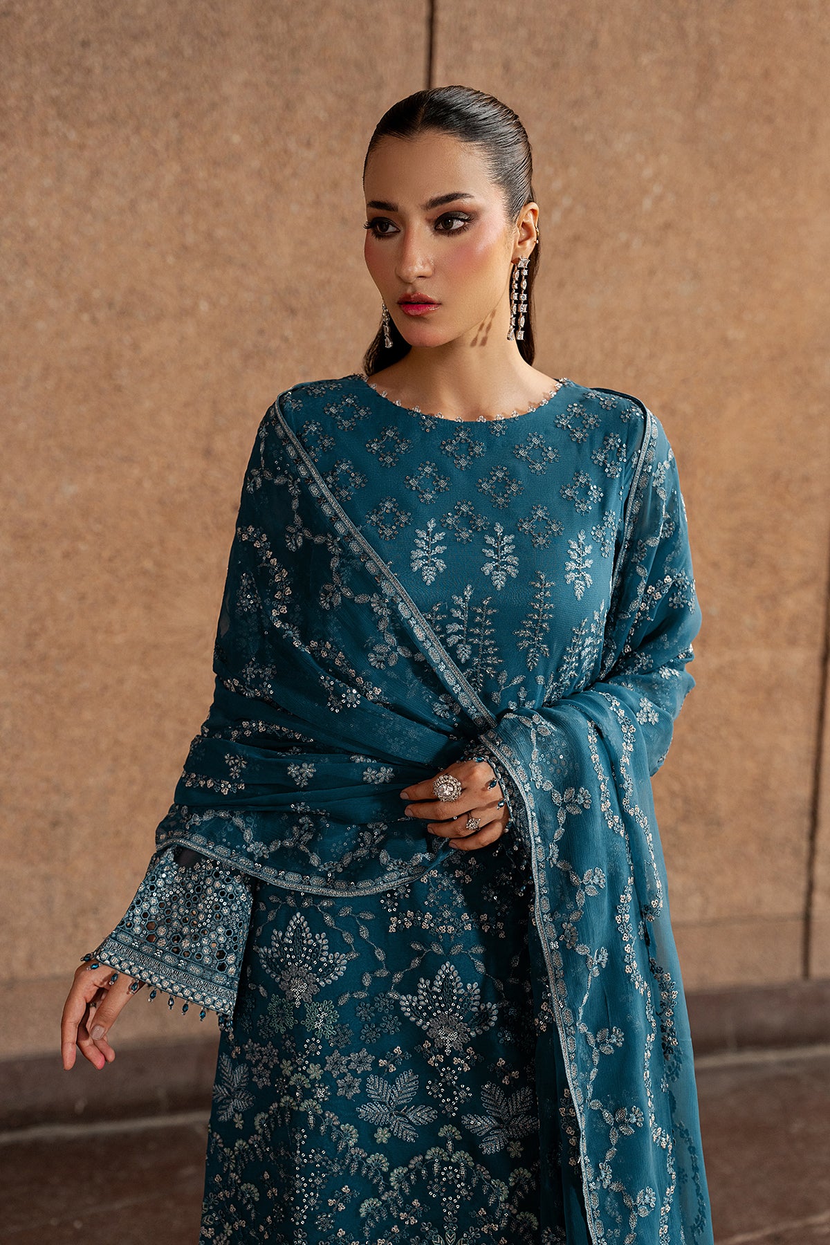 Woman wearing a teal embroidered dress against a beige wall