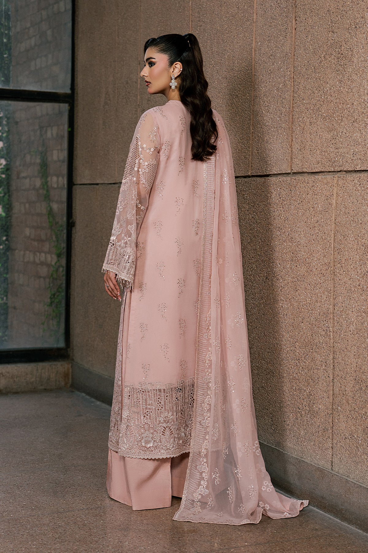 Woman in a pink traditional outfit standing against a textured wall.