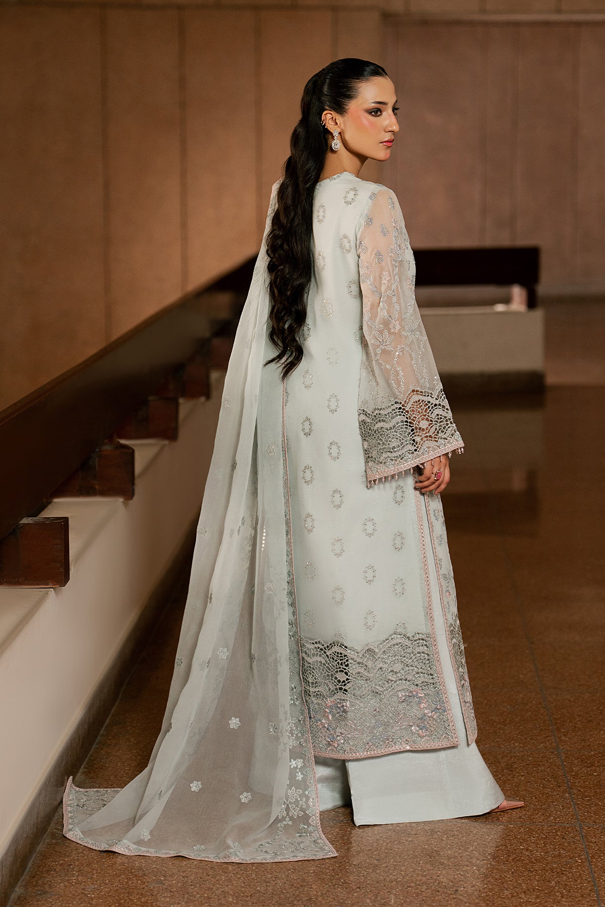 Woman in a white traditional outfit with intricate patterns standing in a room.
