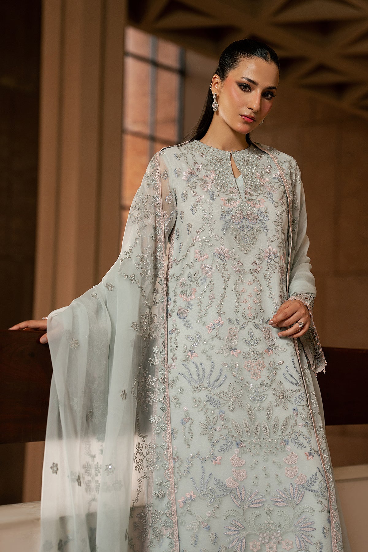 Woman wearing a light gray embroidered traditional outfit with a sheer dupatta.
